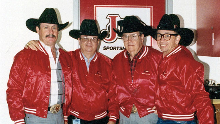 Four men in matching red jackets smile for a picture